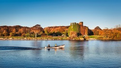 Beautiful scenery of Menlo castle surrounded by a autumn colored trees and boat passing by in Corrib river at Galway, Ireland 
