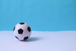 Ball on blue background. Black and white soccer ball or football on a white background. Ball and copy space. Hand holding the ball.