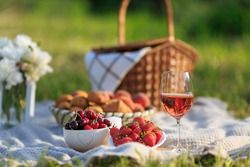 Summertime healthy picnic on nature background at sunny day. Close up Basket fruits strawberries, cherries, glass of red wine, on green grass in garden. Summer weekend outdoor. Beautiful still life