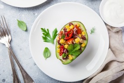 avocado stuffed with quinoa, bean, corn and bell pepper salad on white plate, top view,