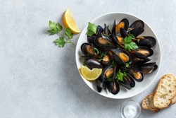cooked mussels with parsley and lemon in white bowl, top view, copy space