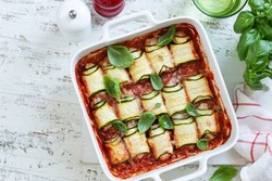 lasagna zucchini rolls with tomato sauce in white baking dish