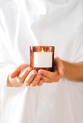 Woman in white clothing holding burning candle close-up. Mock up for candle shop. Space for text or logo branding. Stories format advertising aromatherapy or candle handmade masterclass. Church poster