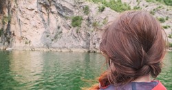 Woman traveler looks at turquoise lake water, moving boat in mountains. Unrecognizable happy woman, back view, ship traveling on green river. Free person. Adventure, travel concept. Explore world