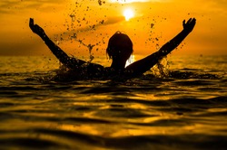 Girl swimming in the sea at sunset, splashes of transparency water, female silhouette