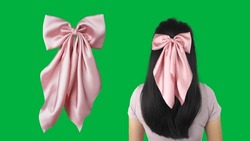 A woman wearing hair bow made out of silk satin fabric with bow design and green background. This beautiful bow with long tails is a great hair accessory.