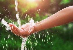 Water pouring splash in hand and nature background with sunshine