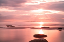 Amazing perfect pink dreamy looking sunset. Slow shutter speed photos of sunset. Smooth water and colorful clody sky. Sunset through straws. Stones on the beach. Wallpaper. Little blur - dreamy look