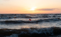 Fishing net location flag in the middle of the waves. Sunset on the background. Small red flag in the sea. Fishing location marked in  in the sea near the beach. Lobster pot location marked. Fishing