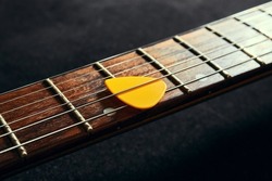 Yellow pick between the strings of an electric guitar close up. Guitar neck with rosewood fingerboard and pick
