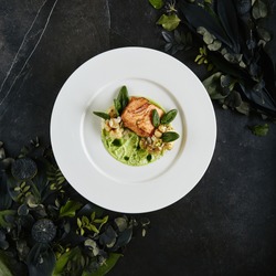 Exquisite Serving White Restaurant Plate with Fillet of Salmon 48 Degrees, Green Peas Cream and Burnt Cauliflower Top View. Stylish Italian Seafood Dish on Natural Black Marble Background