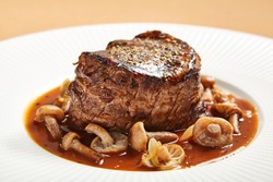 Restaurant meat menu - Filet mignon steak served with mushrooms side view. Beef steak on white plate close-up. Luxury restaurant delicious main course. Fancy roasted meat dish with sauce closeup.