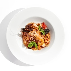 Italian dish - seafood linguine isolated on white background. Pasta with prawn, mussels, octopus,  squid in tomatoes marinara sauce. Seafood pasta in Italian restaurant menu. Seafood on white plate