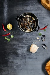 Mussel stew pot with creamy sauce, baguette on stone table. Mussels soup pot contemporary style. Aesthetic composition with seafood. Gastronomy mussel pot dinner concept. Stone table and wooden tray