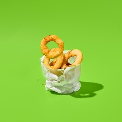 Fried onion rings in paper bag on green background. Flying onion rings in minimal style. Fast food appetizer in contemporary concept. Junk food on color background. Fast food menu