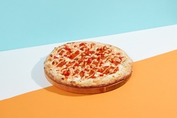 Italian pizza with pepperoni and spicy sauce on coloured background.Spicy pizza with salami, tomato and paprika in minimal style on blue color. American pizza delivery concept with color backdrop