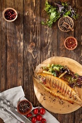 Grilled rainbow trout with herbs on wooden background. Composition with roasted rainbow trout and ingredients. Grilled whole fish on wooden table in rustic style