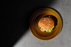 Classic american burger on ceramic plate in dark minimal style. Beef burger on gray stone table with hard shadow. Fast food dark concept. American burger on gray concrete background. Simple food menu