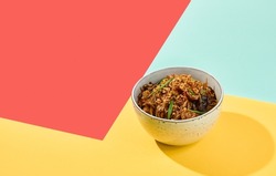Asian fried buckwheat noodles with chicken on coloured background. Fried noodles in ceramic bowl on yellow, red and blue background. Stir-fry soba in trendy style with shadows. Vibrant food
