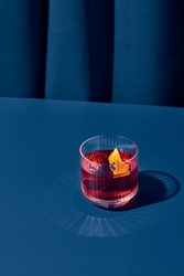Popular cocktail negroni with gin and vermouth on blue background with shadow. Negroni cocktail on coloured background in trendy style. Contemporary concept with alcohol beverage. Bartender cocktail