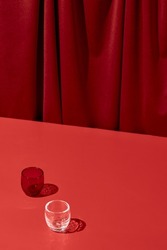 Trendy coloured background with textile. Red background with red table and drapery textile with shadows from glass. Aesthetic red backdrop. Minimal composition with empty place on red background