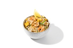 Traditional asian street food - pad thai noodles with shrimp, vegetables and tofu isolated on white background. Pad thai udon with prawns and lemon in ceramic bowl. Fried udon noodles with seafood