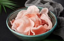 Traditional chinese shrimp crackers in ceramic bowl on black background. Prawn chips in asian style. Prawn crackers in krupuk style with palm leaves. Aesthetic composition with shrimp crackers