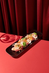Asian appetizer of meat slices, veggies, mushrooms elegantly plated, set against a rich dark red velvet backdrop.