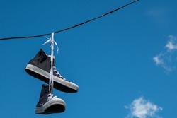 Sneakers hanging on electric wires against a background of blue sky and white clouds.