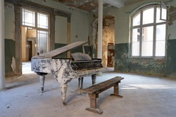 Old dirty black piano with a brown bench in an empty abandoned room - large windows and green walls