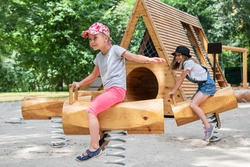 Children riders on wooden swing with spring on the playground in the park. Two girls ride on the playground in summer