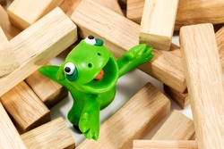 Green plasticine creature looking up standing on a block of wood