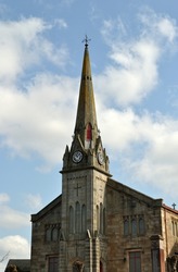 Spire and Clock on Old Stone Church seen against Blue Sky 