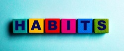 The word HABITS is written on multicolored bright wooden cubes on a light blue background