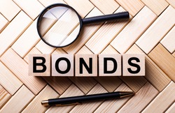 Wooden cubes with the word BONDS stand on a wooden background between a magnifying glass and a handle