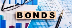 On the bright diagrams, glasses, a pen and wooden cubes with the word BONDS. Business concept