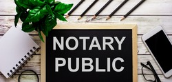 NOTARY PUBLIC is written in white on a black board next to a phone, notepad, glasses, pencils and a green plant.