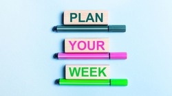 On a light blue background, there are three multi-colored felt-tip pens and wooden blocks with the PLAN YOUR WEEK text.