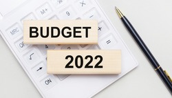 Wooden blocks with the text BUDGET 2022 lie on a light background on a white calculator. Nearby is a black handle. Business concept