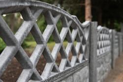 Grey concrete decorative fence somewhere in the park. Blurred green vegetation and tree on the background. Selective focus. Outside landscape