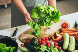 Close Up Photo of Woman Hands Making Fresh Salad on a Table Full with Organic Vegetables. 
An anonymous housewife making lunch with fresh colorful vegetables at kitchen table.