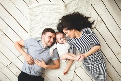 Happy young father, mother and cute baby boy lying on rustic wooden floor