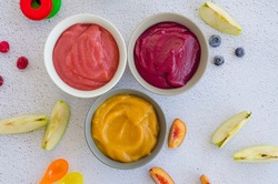 Baby food. Homemade fruit puree. Variety of apple puree or applesauce with frozen peach, raspberries and blueberries in three bowls on a light background. Healthy food. Horizontal. Top view