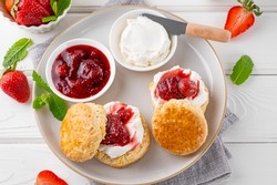 Homemade British Scones with cream cheese, strawberry jam and a cup of tea on a white wooden background