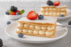 Traditional French dessert millefeuille with vanilla cream and fresh berries on a white plate on a gray concrete background