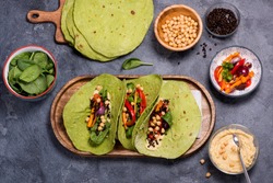 Vegan green tortilla flatbreads or tacos for healthy snack with cheakpeas, hummus, grilled vegetables, beluga lentils and spinach, mexican street food