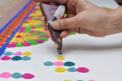 WOMAN HAND MAKING RANGOLI DESIGNS WITH PAPER CONE USING DIFFERENT RANGOLI COLORS
