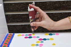 WOMAN HAND MAKING RANGOLI DESIGNS WITH PAPER CONE USING DIFFERENT RANGOLI COLORS on white laminated shoe rack