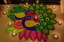 rangoli design of colorful peacock at entrance of the door with small wax tealights diya around it