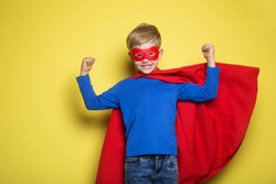 Boy in red super hero cape and mask. Studio portrait over yellow background